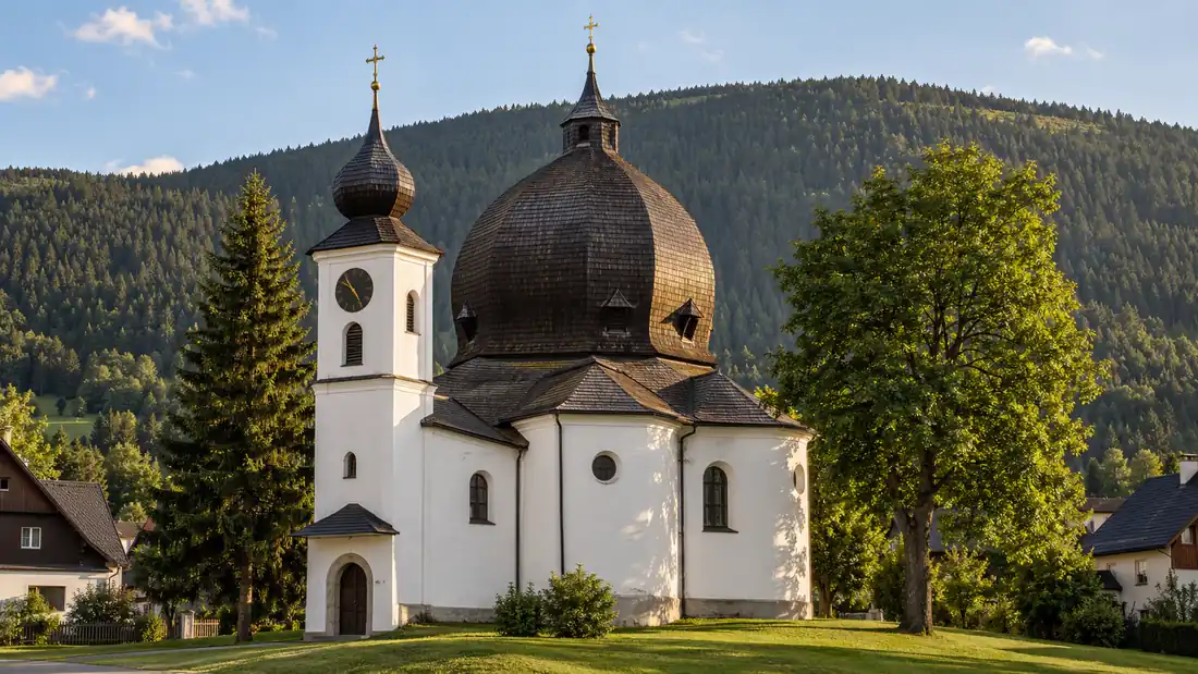 Barokní kostel v Železné Rudě s velkou šindelovou kupolí a bílou věžičkou, za ním zalesněný svah